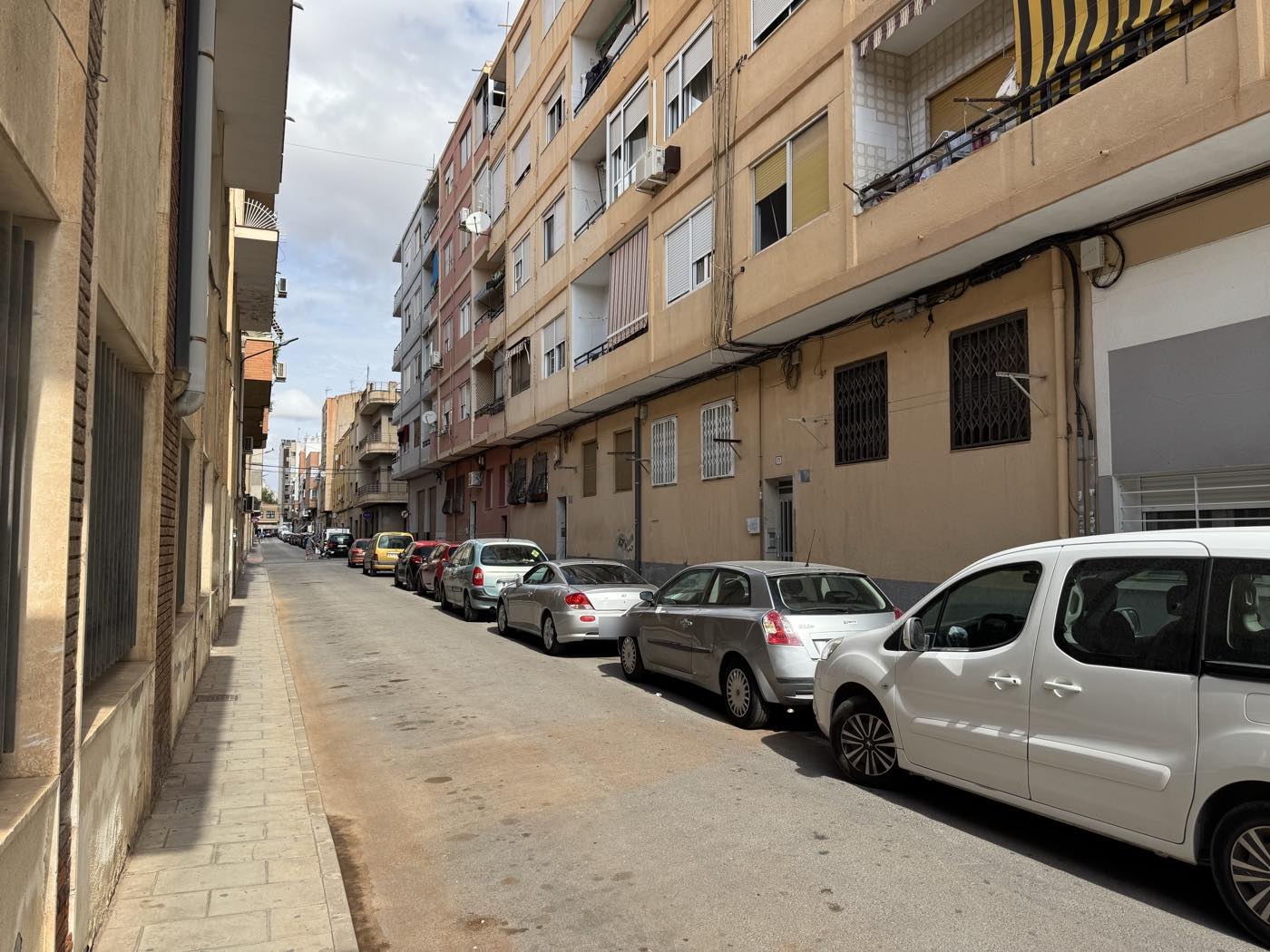 Calle estrecha de Nueva Fraternidad con un bloque de viviendas de cinco plantas, rejas en los bajos y coches aparcados en fila
