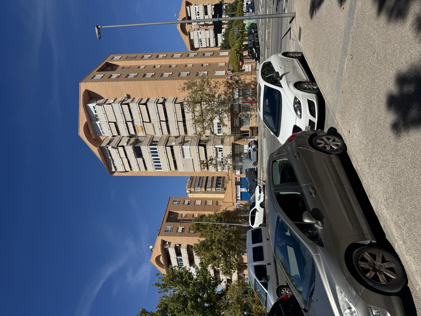Bloques de viviendas de ladrillo en la Avenida de Ronda de Elda, con locales comerciales en los bajos y coches aparcados en la calle
