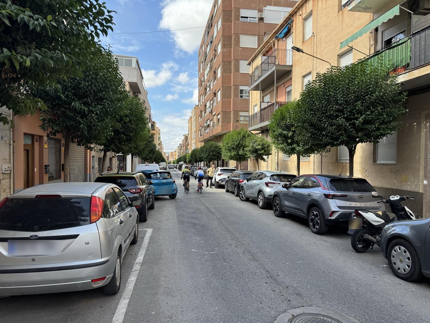 Calle arbolada del barrio de Nueva Fraternidad, en Elda, con bloques de viviendas de cuatro y cinco plantas y coches aparcados a ambos lados