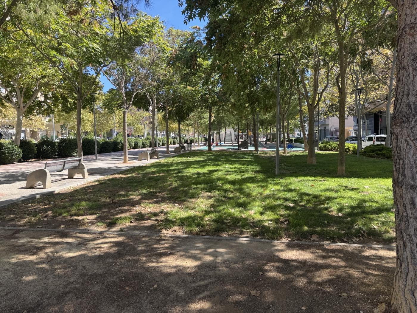 Paseo central de la Avenida de Ronda: césped, arbolado, bancos y zona de juegos infantiles al fondo