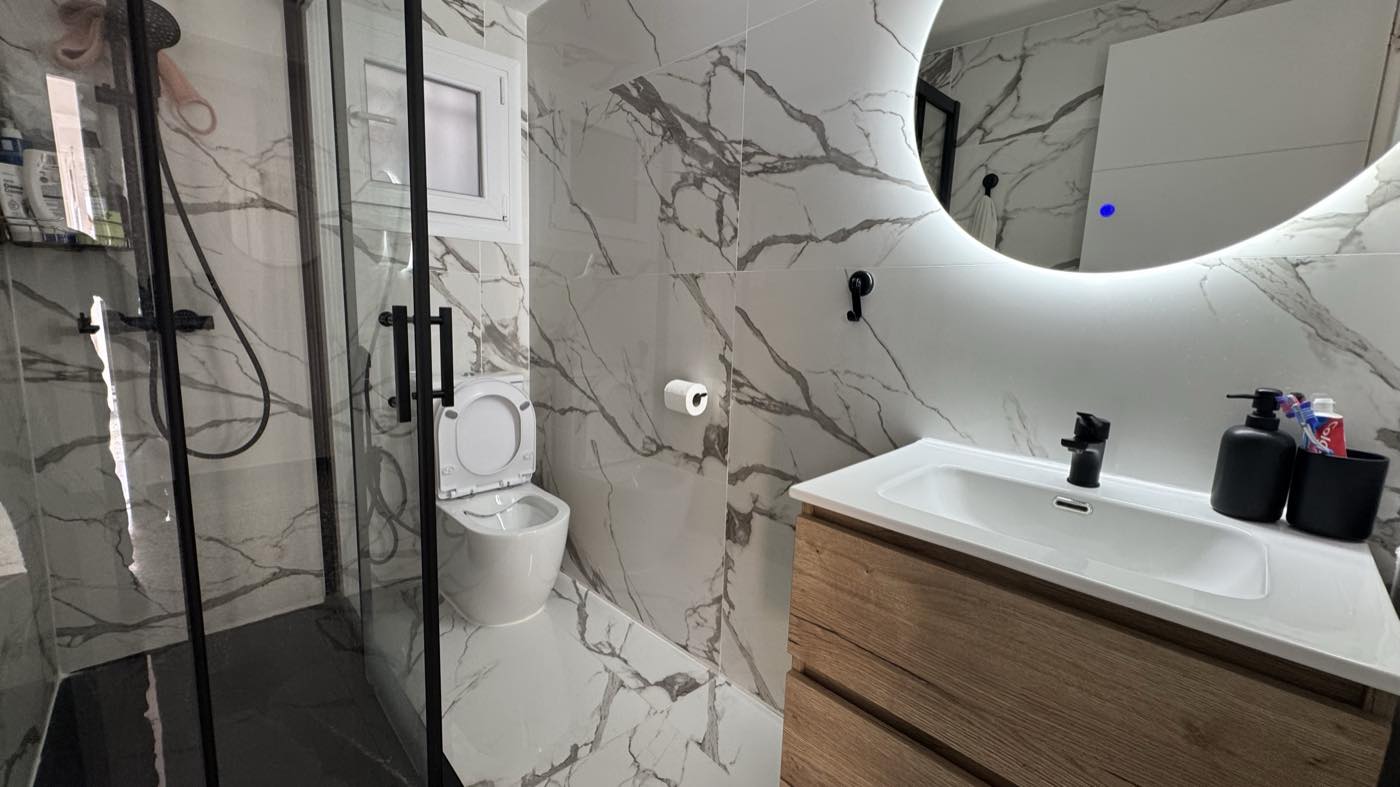 Baño reformado, con plato de ducha, mampara y espejo con luz