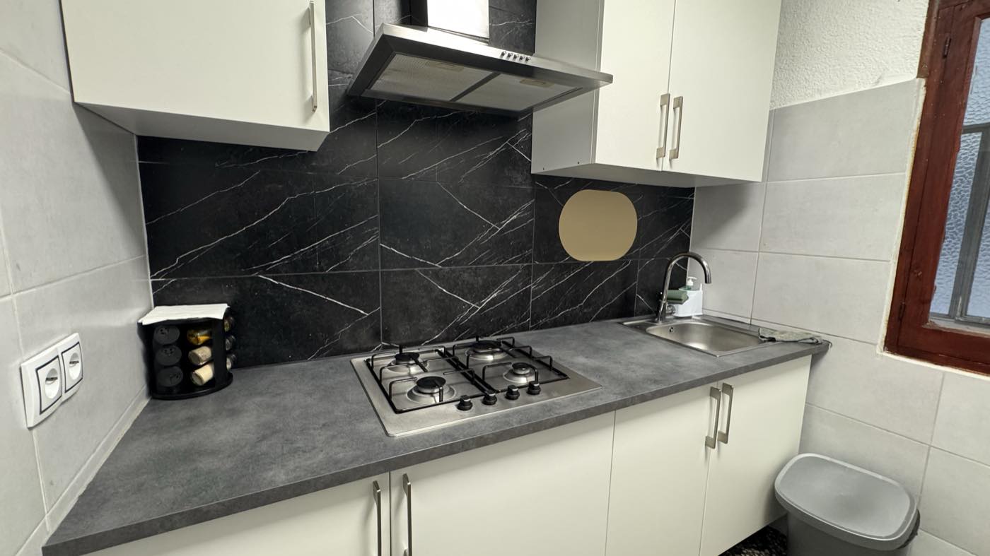 Cocina renovada, con muebles blancos y frente de porcelánico oscuro